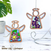 Two Forged Flare® Mother's Angels® 3.5" wooden angel ornaments with stained glass-style centers are shown—one with a water lily, the other a purple larkspur, July’s birth flowers. "July Water Lily & Larkspur" appears below. A plant stand is in back.