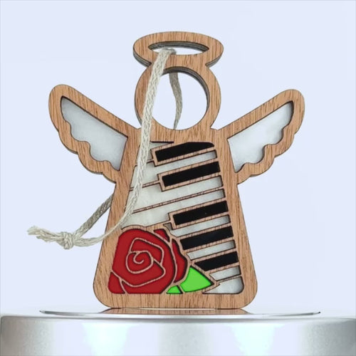 A wooden angel ornament, featuring a clear circular halo and wings, is adorned with black and white piano keys and a red rose on its body. This elegant piano ornament comes with a string for hanging.
