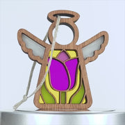 A wooden angel ornament with white wings and a halo, featuring a colorful stained glass–style tulip design. The centerpiece is a vibrant pink flower with green leaves, set against a yellow background. A braided linen string is attached to the ornament.