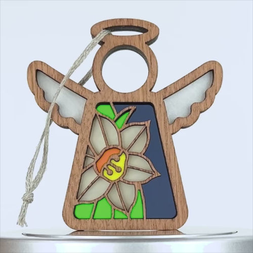 A wooden angel ornament with a stained-glass effect. The body of the angel contains a flower resembling a narcissus with white petals and a yellow center against a blue and green background. A small braided linen string is attached to the ornament for hanging.